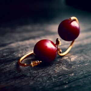 Close-up of red pearl earrings with gold setting on dark wooden background, perfect for fashion and jewelry themes.